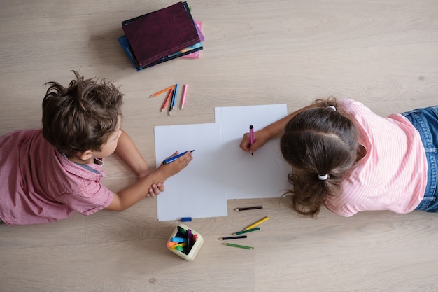 La niña y el niño lindos se relajan estudiando en casa, hacen la tarea en el suelo. Hermana y hermano. Hermanos. Escritura. concepto de educación remota. Cuarentena. Concepto de regreso a la escuela.