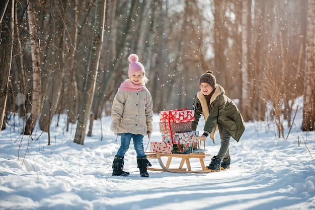 Una niña y un niño llevan el trineo con regalos de Navidad en el fondo de invierno