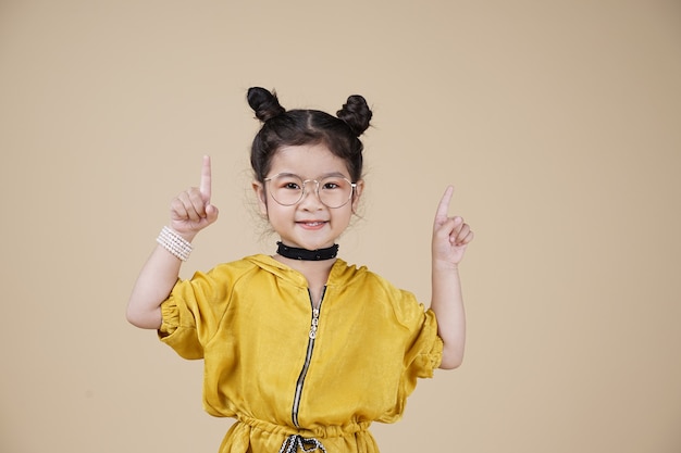 Niña de niño de moda asiática muy sonriente en vestido amarillo sobre fondo beige con espacio de texto libre
