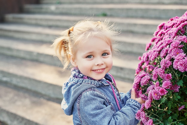 Niña niño en un parque cerca de una cama de flores de crisantemos en otoño