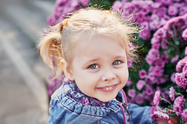 Niña niño en un parque cerca de una cama de flores de crisantemos en otoño