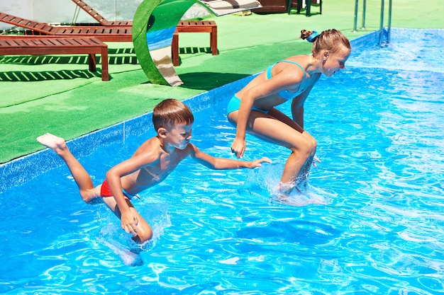 Niña y niño saltando a la piscina del resort