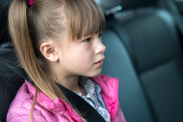 Niña niño sentado en un automóvil en el asiento trasero abrochado con cinturón de seguridad.