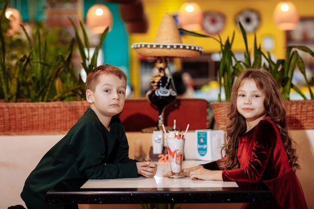 Niña y niño sentados en una mesa en un café con un batido