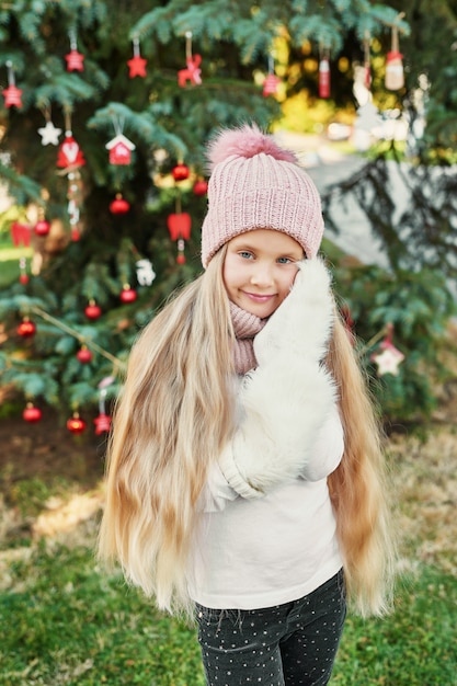 niña niño en un sombrero y bufanda cerca del árbol de Navidad