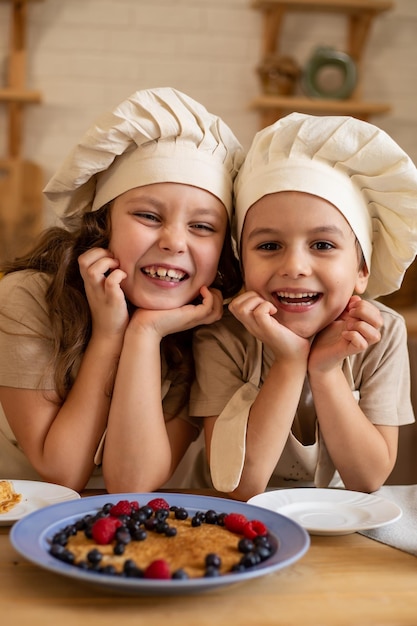 niña y niño con sombreros y delantales de chef están sentados en una mesa de madera riéndose alegremente