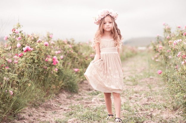 Niña niño sonriente posando en el jardín de rosas con un vestido elegante