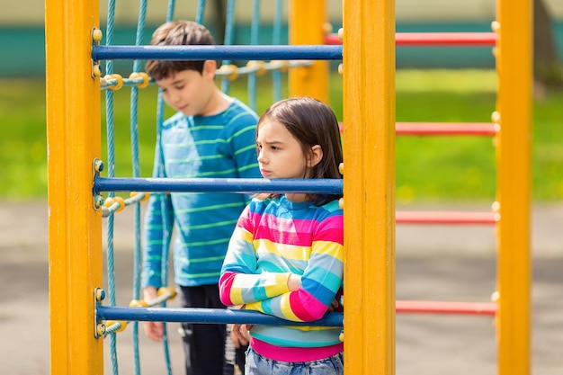 Una niña y un niño tristes y aburridos se paran entre el patio de recreo amarillo y colorido del parque