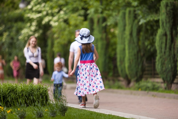 Niña niño vestido de verano y un sombrero caminando solo en el parque verde.