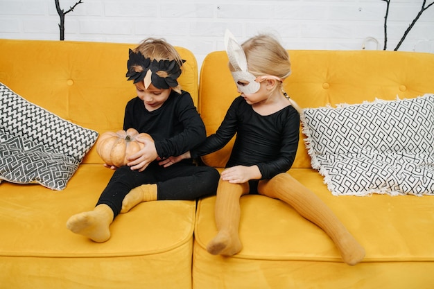 Niña y niño vestidos para halloween en un sofá jugando con calabaza