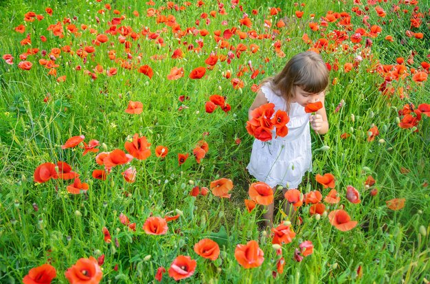 Niña de los niños en un campo con enfoque selectivo de amapolas