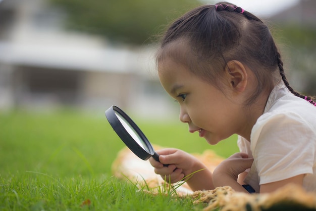 La niña de los niños está mirando las hojas de los árboles a través de la sesión al aire libre de la lupa