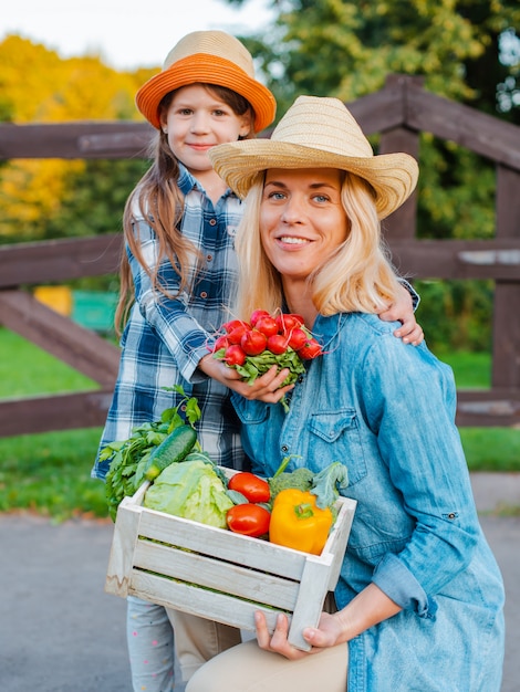 Niña de los niños que detiene a mamá una cesta de verduras orgánicas frescas con el huerto.