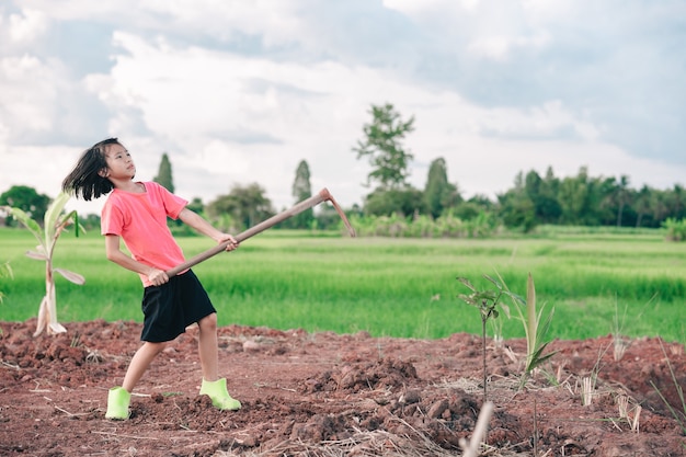 Niña de niños sosteniendo azada y cavar tierra para plantar árboles en el jardín