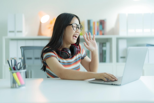 Una niña o estudiante que usa una computadora portátil en la biblioteca mientras usa anteojos y auriculares Ella sonríe y se ve feliz