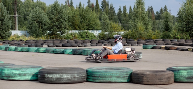 Una niña o una mujer con casco monta un kart en una pista especial cercada con ruedas de goma. Recreación activa y deportes en el transporte. Preparación y entrenamiento para competiciones.