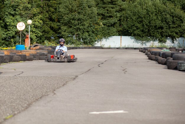Una niña o una mujer con casco monta un kart en una pista especial cercada con ruedas de goma. Recreación activa y deportes en el transporte. Preparación y entrenamiento para competiciones.