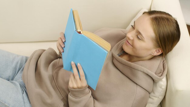 Foto niña o mujer joven leyendo un libro acostado en el sofá