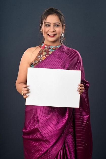Una niña o una mujer que lleva un sari tradicional indio sosteniendo un cartel en sus manos sobre fondo gris