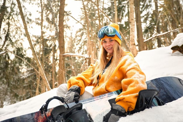 Niña o mujer snowboarder entra para deportes de invierno en el bosque nevado que se encuentra en la nieve y sostiene una tabla de snowboard