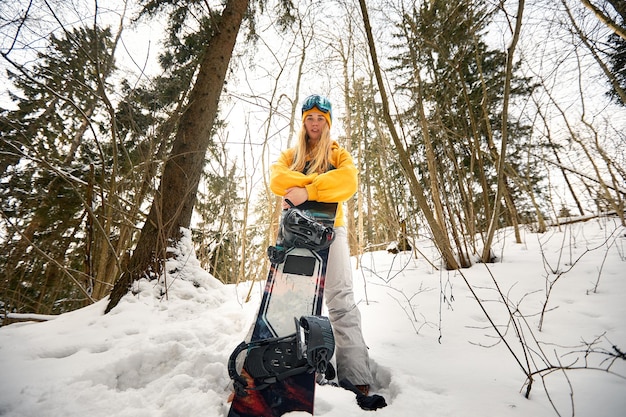 Niña o mujer snowboarder entra para deportes de invierno en el bosque nevado que se encuentra en la nieve y sostiene una tabla de snowboard