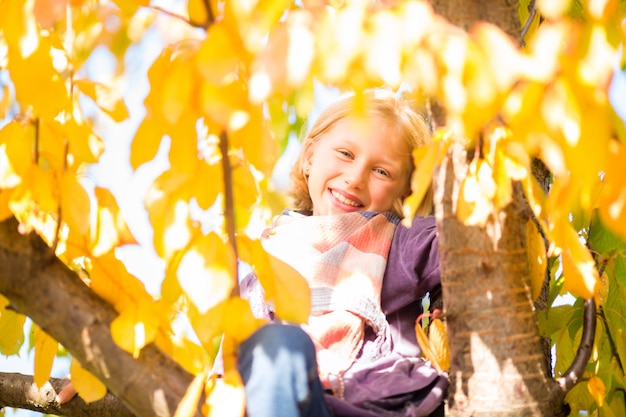 Niña o niño en árbol en otoño o otoño colorido