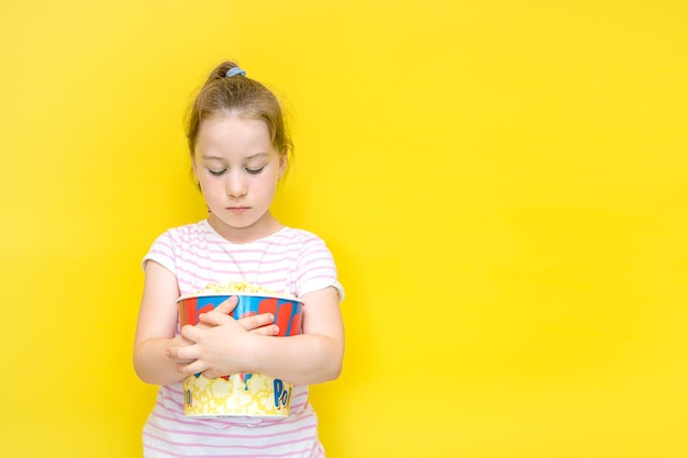 Niña ofendida con ambas manos agarra un enorme vaso de palomitas de maíz con espacio para copiar