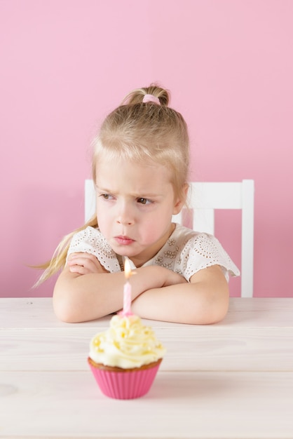 Niña ofendida con un cupcake con una vela sobre un fondo rosa