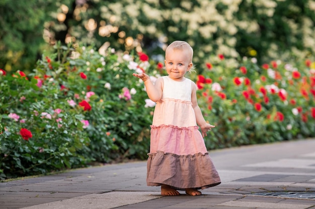 Niña de ojos azules camina en un jardín floreciente en verano con un vestido largo de lino vintage