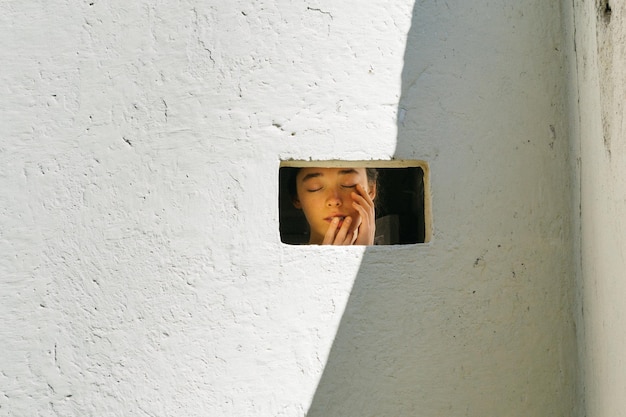 Niña con los ojos cerrados vista a través de la ventana
