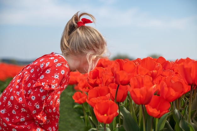 Una niña olfateando tulipanes en un campo rojo.