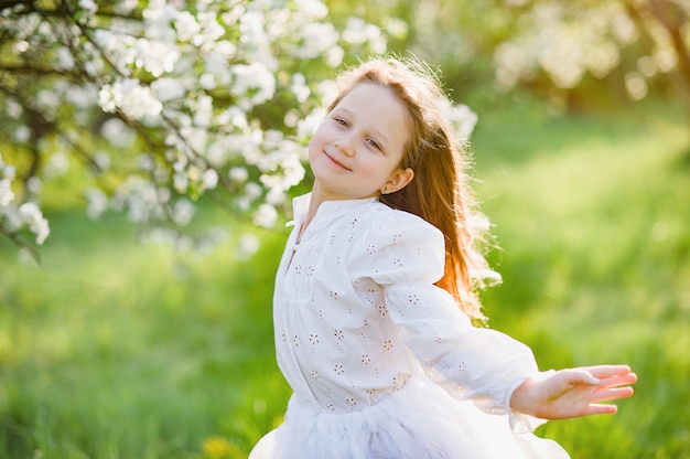 Niña oliendo flores de huerto de manzanas. Jardín con árboles en flor.