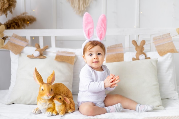 Niña en orejas de conejo en la cama en casa con huevos pintados y conejo concepto de pascua lindo bebé de Pascua está esperando las vacaciones y regocijándose