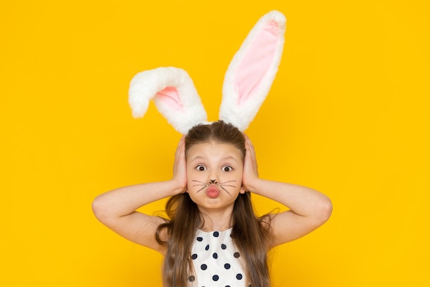 Una niña con orejas de conejo de Pascua hinchó las mejillas y se agarró la cabeza con las manos.