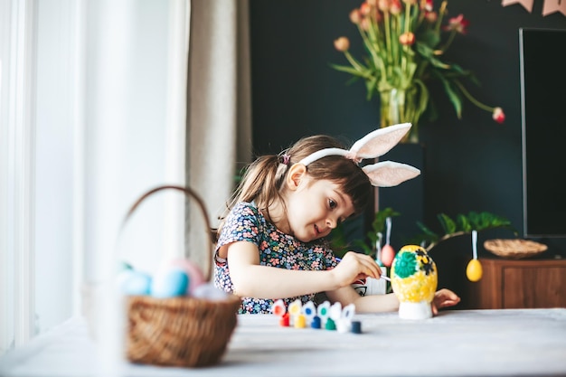 Niña con orejas de conejo pintando huevos de Pascua de yeso con pincel