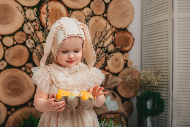 Niña con orejas de conejo y sentada con patitos blancos en el fondo de madera