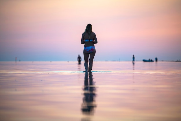 Una niña en la orilla del mar al atardecer camina sobre el agua