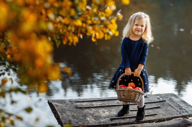 Niña en otoño con una cesta de manzanas.