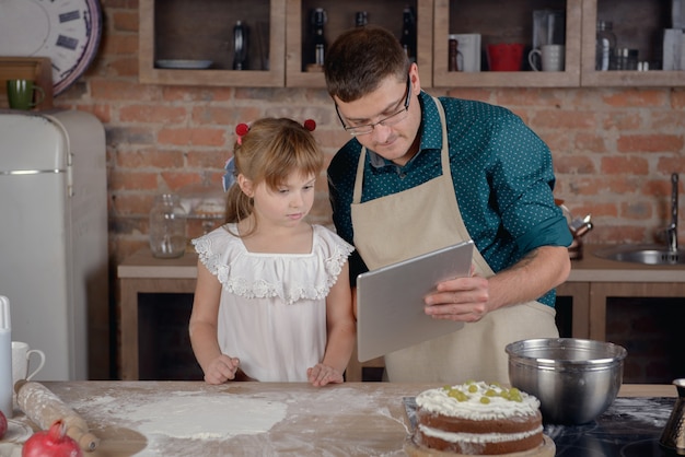 Niña con padre en la cocina con tableta digital