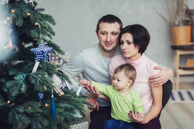 Niña con padres decorando el árbol de Navidad