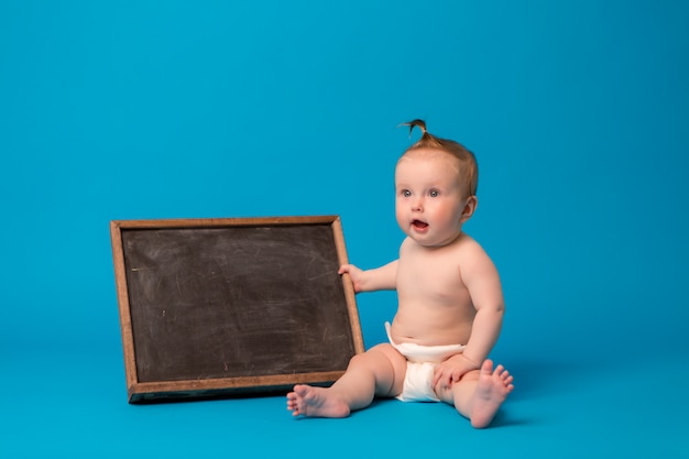 niña en pañales sosteniendo un tablero de dibujo sobre un fondo azul