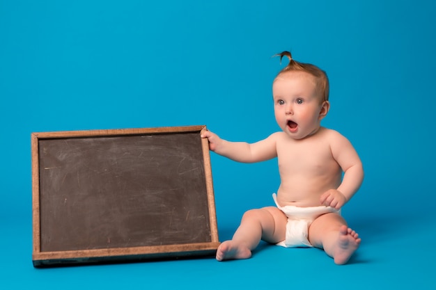 niña en pañales sosteniendo un tablero de dibujo sobre un fondo azul