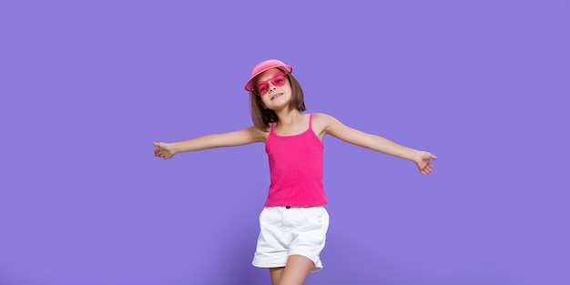 Una niña con pantalones cortos blancos, una camiseta rosa, gafas de moda rosas y una visera de verano.