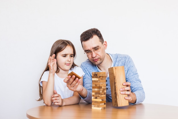 Niña y papá juegan un juego en casa, cuestan una torre de bloques, cubos, jenga, rompecabezas para el desarrollo del cerebro, inteligencia mental