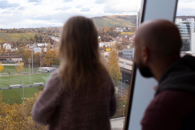 Niña y papá de pie con la espalda mirando por la ventana panorámica