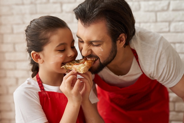 Niña y papá que prueban la rebanada de la pizza con la mordedura.