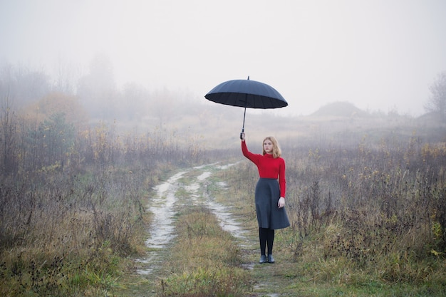 Niña con paraguas en campo de otoño