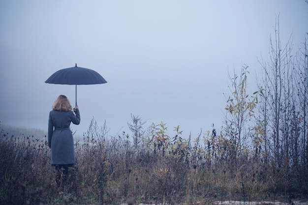 Niña con paraguas en campo de otoño