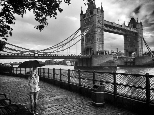 Niña con paraguas de pie junto al puente de la torre