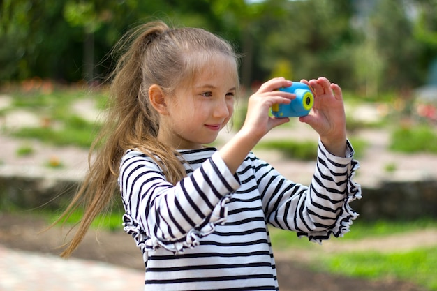 Una niña en el parque en un día soleado tiene una pequeña cámara y toma fotografías